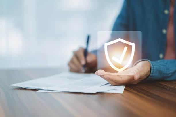 a person signing on some paper with a shield with check  icon on his hand