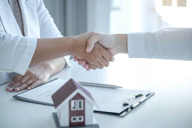 a professional handshake between two people with some files and a model house on the table