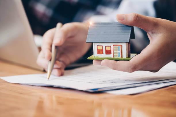 a person signing a contract with a small house model in hand