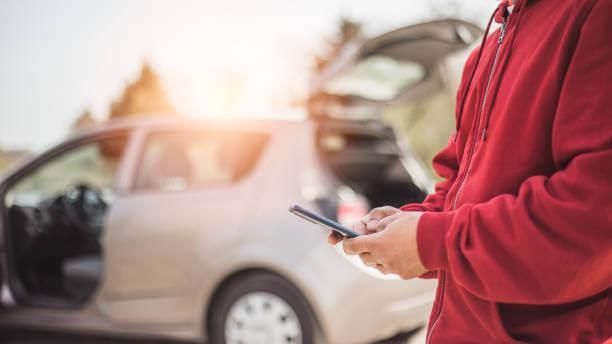 a person holding a phone next to a broken car