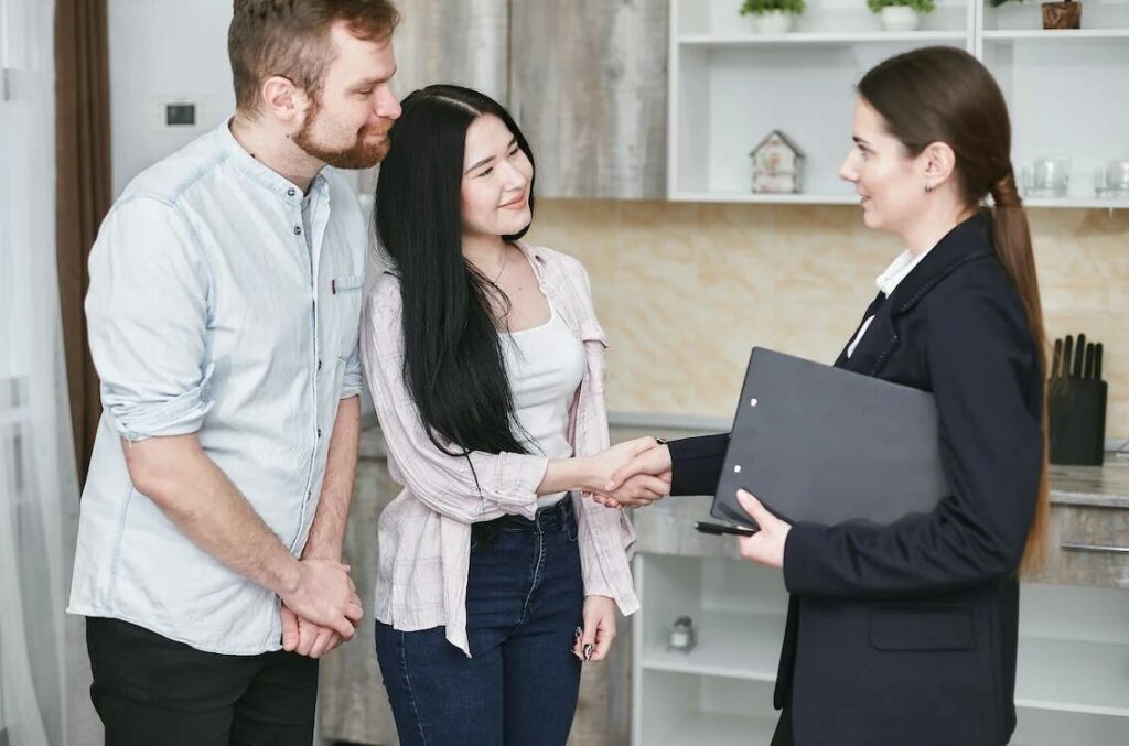 a man standing beside a woman, shaking the hand of another woman in business attire