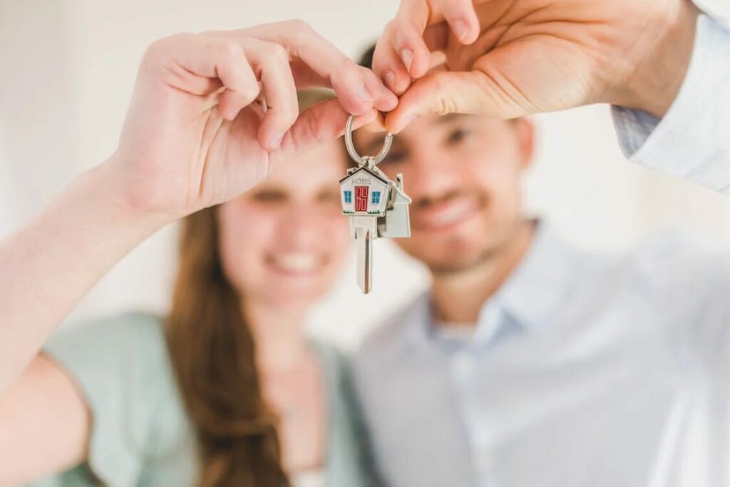 a couple holding up a key with a house keychain while smiling