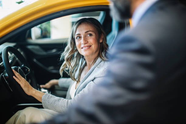 a woman sitting in her car with the door open while smiling at a man